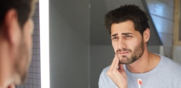 Man next to bathroom mirror holding his cheek in pain