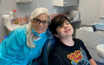 Dental team member smiling next to teenage boy in dental chair
