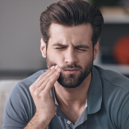 Wincing man holding his cheek in pain needing an emergency dentist in Mercerville