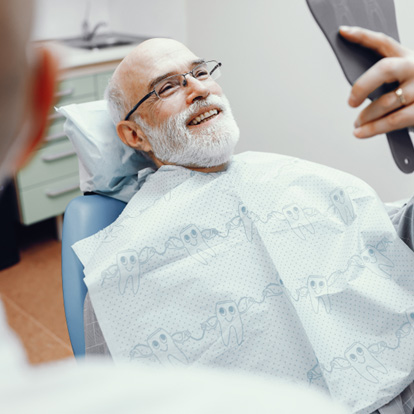 Mercerville patient smiling in mirror after getting implant dentures 