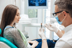 Dentist holding a model dental implant while talking with patient