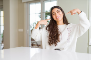 Woman sitting in her kitchen and pointing at her bright smile